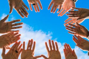 Groupe de mains étendues vues du dessous, sur fond de ciel bleu